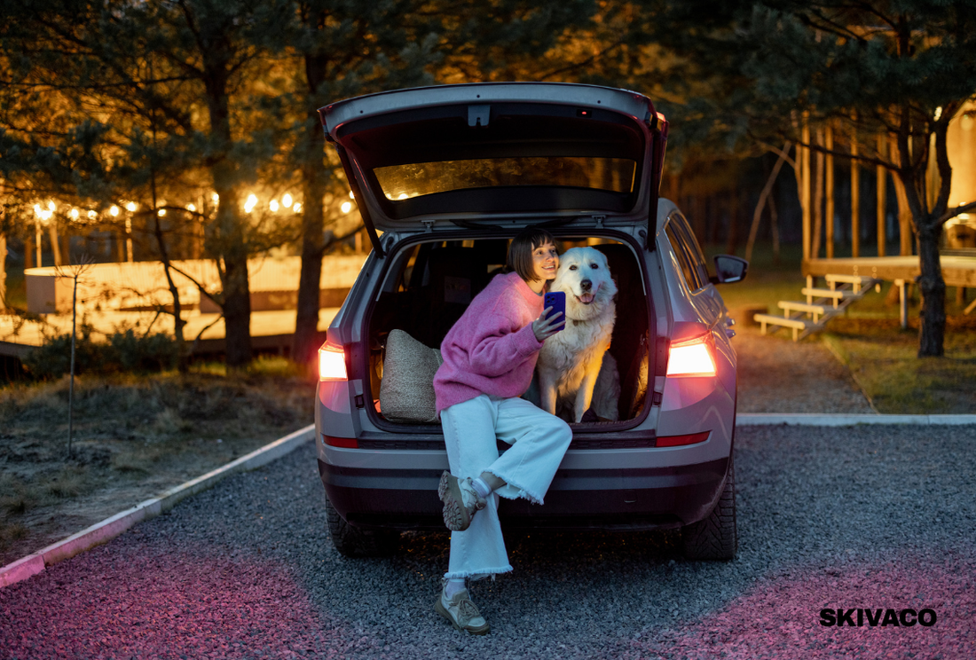 Pet parent traveling with a dog, sitting in the open trunk of a car during an outdoor road trip